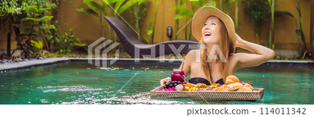BANNER, LONG FORMAT Breakfast tray in swimming pool, floating breakfast in luxury hotel. Girl relaxing in the pool drinking smoothies and eating fruit plate, smoothie bowl by the hotel pool. Exotic 114011342
