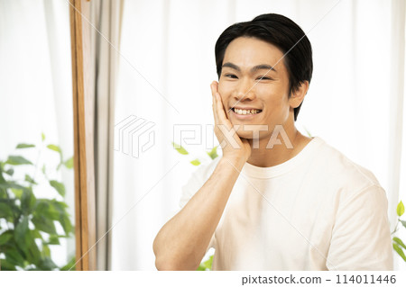 一個男人一邊照鏡子一邊做皮膚護理 一個男人一邊照鏡子一邊做皮膚護理 114011446