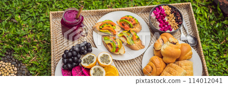 BANNER, LONG FORMAT Breakfast on a tray with fruit, buns, avocado sandwiches, smoothie bowl standing on the grass BANNER, LONG FORMAT Breakfast on a tray with fruit, buns, avocado sandwiches, smoothie bowl standing on the grass 114012041