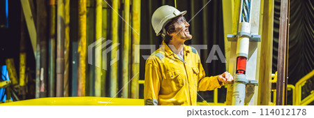 Young man in a yellow work uniform, glasses and helmet in industrial environment,oil Platform or liquefied gas plant BANNER, LONG FORMAT 114012178