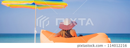 Summer lifestyle portrait of pretty girl sitting on the orange inflatable sofa on the beach of tropical island. Relaxing and enjoying life on air bed BANNER, LONG FORMAT 114012216
