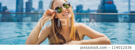Young woman in outdoor swimming pool with city view in blue sky BANNER, LONG FORMAT 114012836