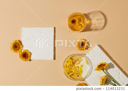 Stone podiums in white color arranged with some fresh flowers, a beaker and a petri dish filled with oil extracted from Calendula flowers. Minimal scene with geometric podium platform 114013231