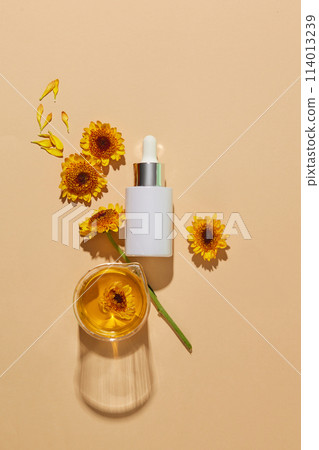Unlabeled glass serum bottle arranged with a beaker of Calendula flower oil over beige background. Calendula is an annual plant that thrives in almost any soil. Mockup design 114013239