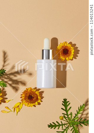 Flat lay of green leaves and Calendula flowers displayed around an unbranded glass serum bottle. Natural cosmetic concept. Empty label for branding mockup  114013241