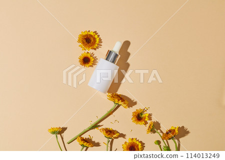 Empty label serum bottle decorated against the background in beige color with fresh Calendula flowers. Calendula extract is known for its antifungal and antibacterial properties 114013249