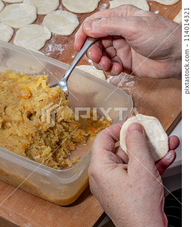 Woman hands are making a damp dumpling. On the wooden counter 114014321