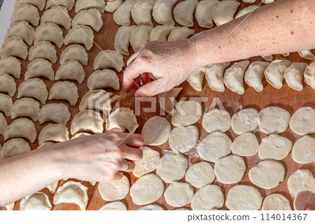 Female hands are making a damp dumpling. On the wooden counter 114014367