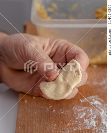 Woman hands are making a damp dumpling. On the wooden counter 114014395