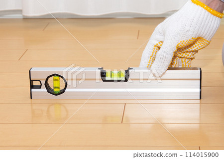 A worker uses a level to check the level of a floor 114015900