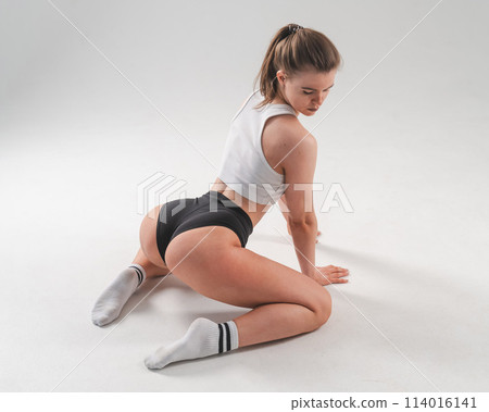 A woman in shorts sits with her back on a white floor. Beautiful butt. Vertical photo. A woman in shorts sits with her back on a white floor. Beautiful butt. Vertical photo. 114016141