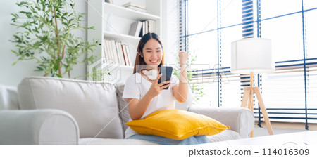 Happy young asian woman relax on comfortable couch at home texting messaging on smartphone Happy young asian woman relax on comfortable couch at home texting messaging on smartphone 114016309