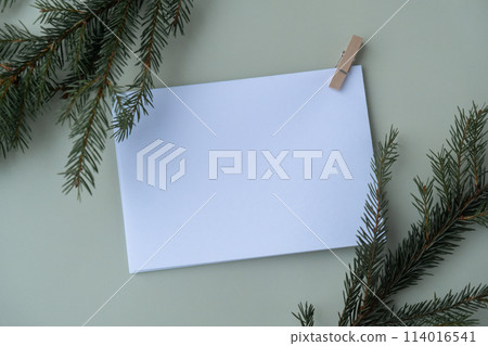 Green background with Christmas tree branch decor and copy space mock up white envelope. Template for Christmas greeting card New Year postcard. Flat lay 114016541