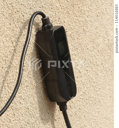 Portable charging box in cable for electric car charging on a gray wall. 114018865