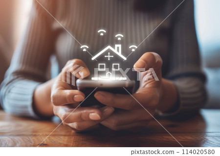 A woman is holding a phone with a house icon on it 114020580