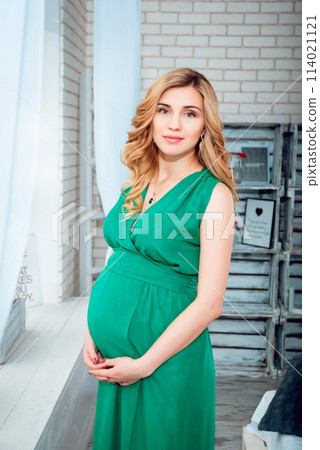 Young pregnant woman near a window. Background Young pregnant woman near a window. Background 114021121