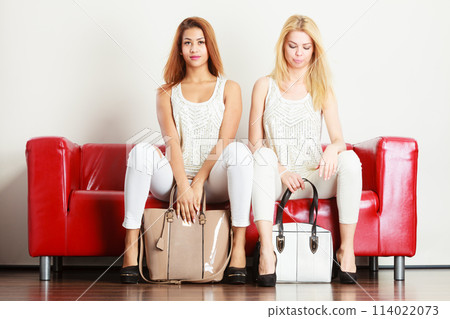 Two women sitting on sofa presenting bags Two women sitting on sofa presenting bags 114022073