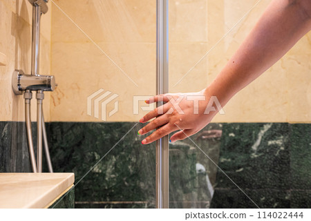 A hand with fingers extended reaches out to open a glass shower door A hand with fingers extended reaches out to open a glass shower door 114022444