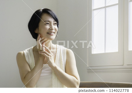 Portrait of a middle-aged woman sitting by the window in the living room Beauty 114022778