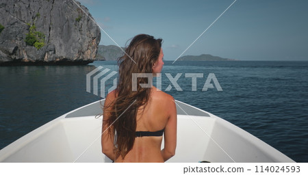 A woman wearing a bikini is seated in a boat, possibly on a boat tour around the El Nido Islands in the Philippines. The boat appears to be moving slowly. 114024593