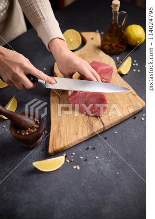 Woman cut tuna steak into slices on a wooden cutting board at domestic kitchen cooking tuna carpaccio Woman cut tuna steak into slices on a wooden cutting board at domestic kitchen cooking tuna carpaccio 114024796