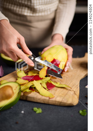 Woman peeling mango on a wooden cutting board at domestic kitchen 114024804