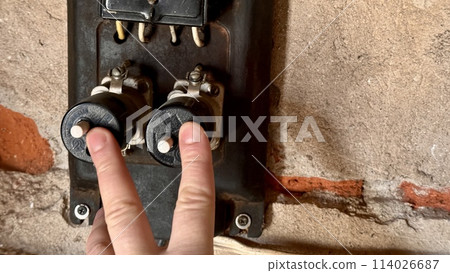 An antique household electricity meter with push-button type electric fuses in the garage. The man's fingers turn off the fuses. Close-up An antique household electricity meter with push-button type electric fuses in the garage. The man's fingers turn off the fuses. Close-up 114026687