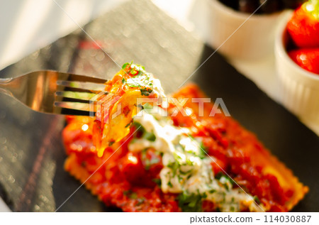 Four cheese filled ravioli in a tomato and basil sauce on the black stone plate 114030887