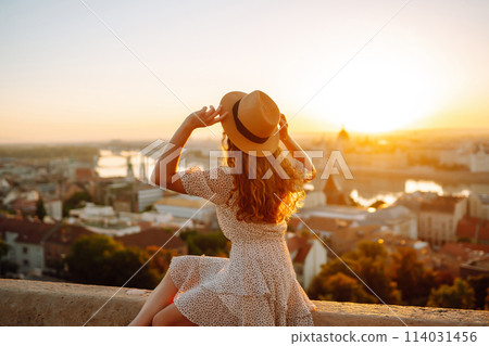 Young female tourist enjoys view of city at sunset. back view Lifestyle, travel, nature, active life Young female tourist enjoys view of city at sunset. back view Lifestyle, travel, nature, active life 114031456