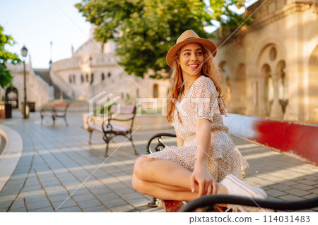 Happy young woman in hat at dawn enjoys view of beautiful buildings. Lifestyle, recreation concept. 114031483