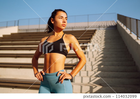 Young woman in sports outfit doing exercises outdoors in the morning. Woman doing stretching exercise. 114032099