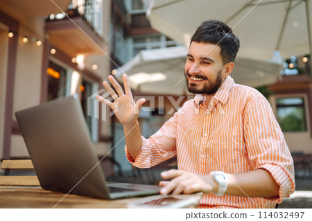 Happy male freelancer smiling while working at laptop with phone, online conference. Blog concept. Happy male freelancer smiling while working at laptop with phone, online conference. Blog concept. 114032497