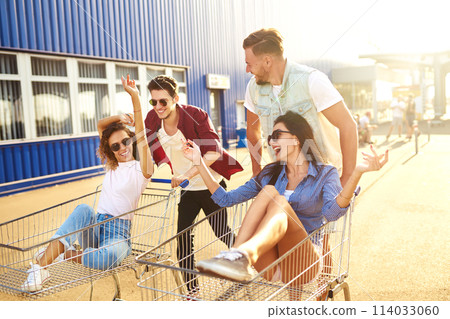Group of happy young people having fun on shopping trolleys. Multiethnic young people racing on shopping cart. Group of happy young people having fun on shopping trolleys. Multiethnic young people racing on shopping cart. 114033060