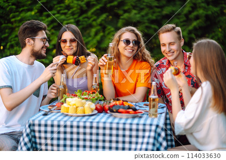 Happy friends in picnic in park. Friends grill meat, have fun, relax. ?oncept of holidays, weekends. Happy friends in picnic in park. Friends grill meat, have fun, relax. ?oncept of holidays, weekends. 114033630