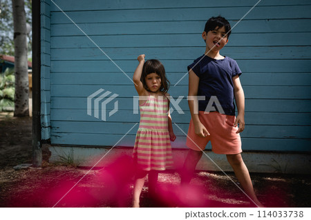 two children playing making funny faces in front of blue house two children playing making funny faces in front of blue house 114033738