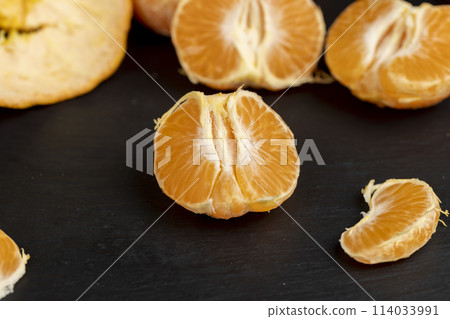 a large number of orange citrus fruits on a black slate surface 114033991