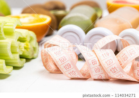 Measuring tape and bottled smoothie among vegetables and fruits. Proper nutrition and weight loss concept. Measuring tape and bottled smoothie among vegetables and fruits. Proper nutrition and weight loss concept. 114034271