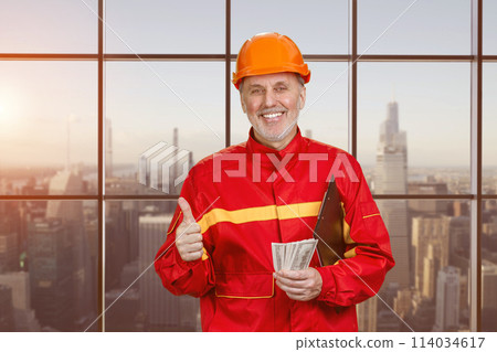 Portrait of happy elder man holding money and showing like gesture. WIndows with view of urban cityscape background. Portrait of happy elder man holding money and showing like gesture. WIndows with view of urban cityscape background. 114034617