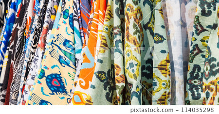 Uzbek dresses and female clothes made of silk and cotton with a colorful pattern at oriental bazaar close up 114035298