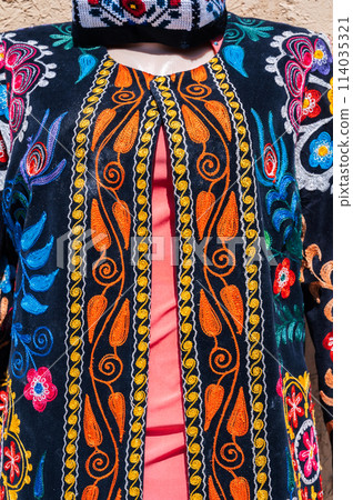 Traditional Uzbek festive dress with multicolored floral embroidery at oriental bazaar in Uzbekistan close up Traditional Uzbek festive dress with multicolored floral embroidery at oriental bazaar in Uzbekistan close up 114035321