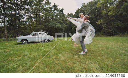 Bride and groom twirling in the background of a retro automobile. 114035368