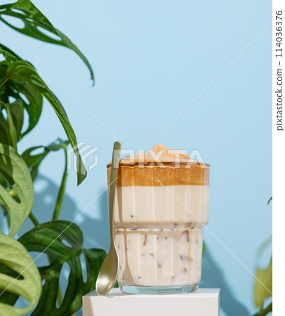 Dalgona coffee. Whipped instant coffee in a glass on a white stand with coffee beans  114036376