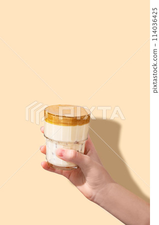 Dalgona coffee. A hand holds a glass of whipped and instant iced coffee and milk in a glass  114036425