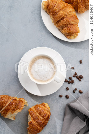 A cup of aromatic cappuccino coffee and fresh croissants on a blue background. A cup of aromatic cappuccino coffee and fresh croissants on a blue background. 114036467