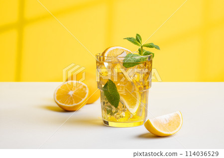 A glass of iced tea with lemon and mint on a yellow and white background with a shadow 114036529