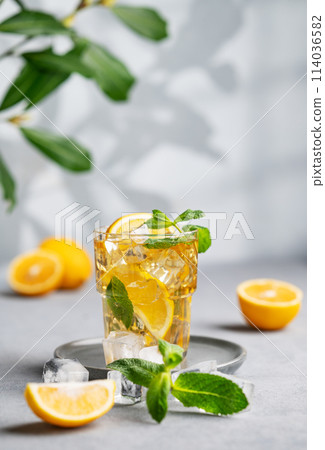 Iced tea with lemon, mint and ice in a glass on a light background with shadow and branch. Iced tea with lemon, mint and ice in a glass on a light background with shadow and branch. 114036582