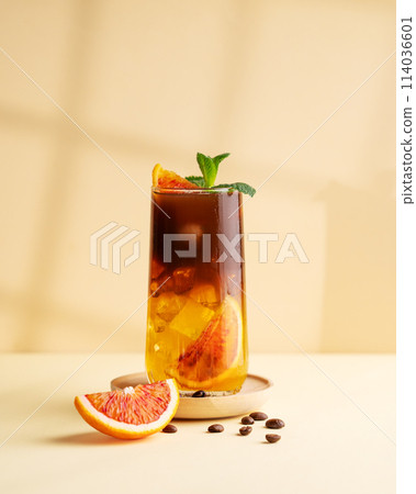 Americano coffee with orange juice (bumble) in a tall glass with ice and mint on a yellow background Americano coffee with orange juice (bumble) in a tall glass with ice and mint on a yellow background 114036601