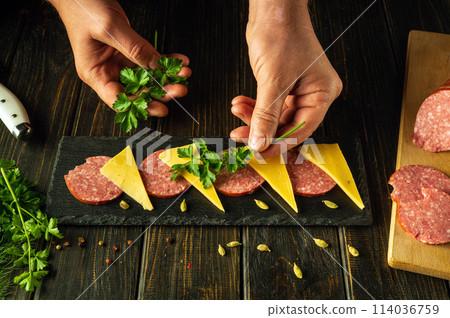 Serving food. The cook places parsley on the serving board with his hands to add flavor to the cheese and sausage appetizer. Place for advertising 114036759