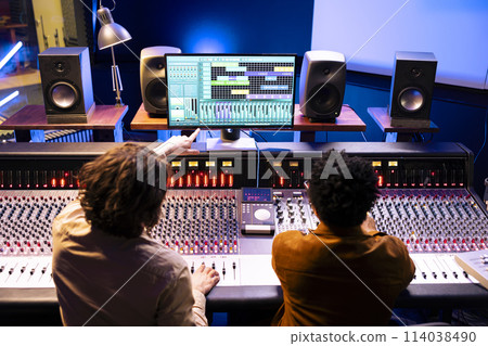 Audio engineer and artist collaborating on new songs for pop album, composing and editing tunes with mixing console and digital software. Musician working with technician on records in studio. 114038490