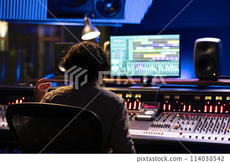 Audio expert working on editing music with daw software interface, processing and mixing sounds in control room. Skilled engineer operating on control panel board console, mixer station. 114038542